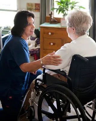 Nurse helps woman sitting in a wheelchair in her living room.