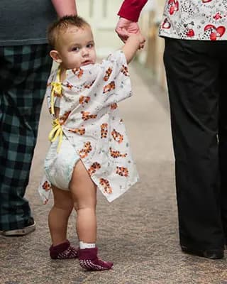 Toddler in hospital gown walks with adult