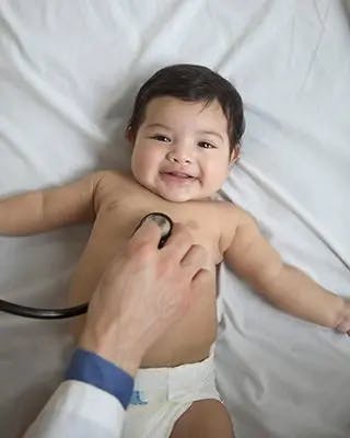 Hand holds stethoscope to smiling baby