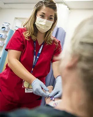 Nurse handles infusion equipment in patient's arm.