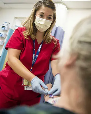 Nurse handles infusion equipment in patient's arm.